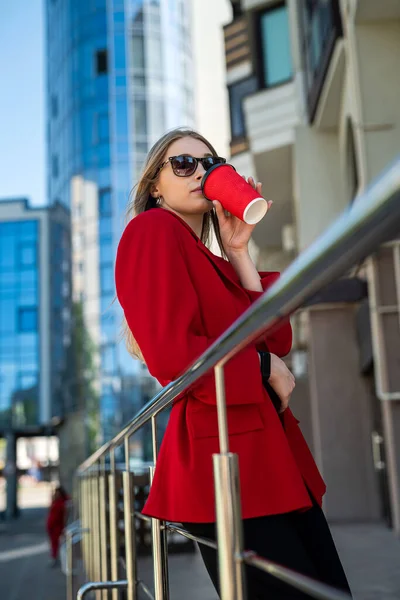 A business woman with a cup of coffee is talking on her smartphone while standing in the middle of the city center. The concept of a woman who earns money