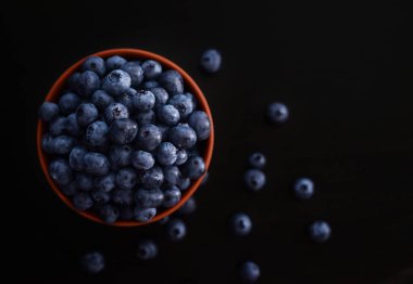 Koyu arkaplanda turuncu kasede yabanmersini. Üst görünüm, metin için boş alan.