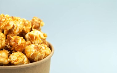 Kağıt bardakta karamelize patlamış mısır. Yakın çekim, makro fotoğrafçılık. İkiye bölünmüş. Sağ taraftaki metin için boş alan.