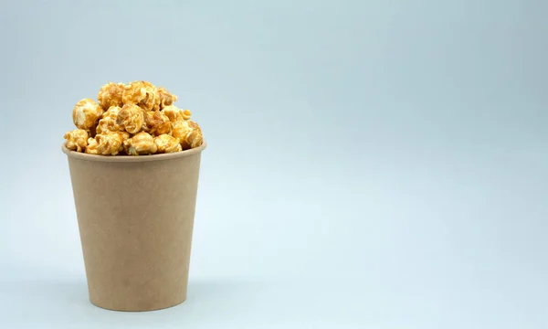 Craft paper cup with popcorn. Caramel popcorn. There is free space on the paper cup, mockup.  Eco concept, no plastic. Free space for text on the right.