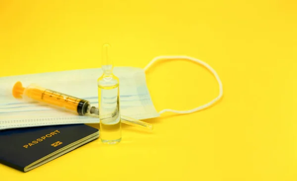The concept of vaccination and travel. International passport, mask,syringe and ampoule with a medicinal substance (vaccine).Yellow background.Traveling during COVID-19 pandemic.
