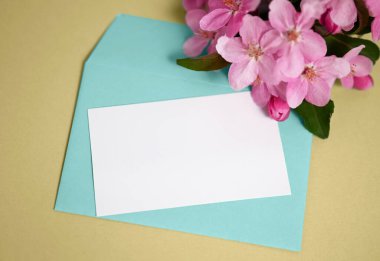 Bahar kompozisyonu. Zarflı ve boş kartlı bir model. Sarı arka planda turkuaz bir zarf ve bir elma ağacının çiçek açan dalı..