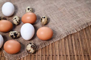 Different types of eggs. Chicken and quail eggs on the table. Bamboo mat, burlap. Top view, place for text. Easter or healthy food concept. Shallow depth of field, selective focus.