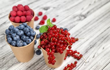 Yaz kompozisyonu. Kağıt bardaklarda sulu yaz meyveleri. Yabanmersini, kırmızı frenk üzümü, ahududu. Hafif ahşap arkaplan.