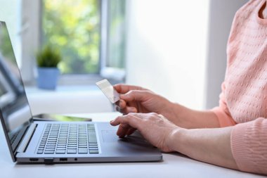 Olgun kadın evde dizüstü bilgisayarla çalışıyor. O, elinde kredi kartı tutuyor. Elleri yakın çekim, gündelik kıyafet. Çevrimiçi alışveriş, evden iş ve serbest konsept.