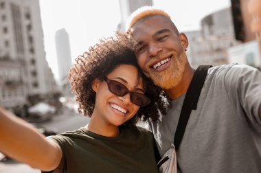 Mutlu bir çift sokakta selfie çekiyor ve mutlu görünüyorlar.