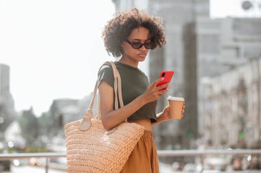 Koyu tenli, güneş gözlüklü, akıllı telefonlu genç bir kadın.