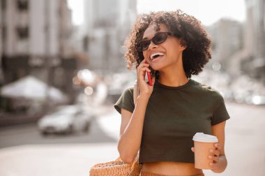 Koyu tenli, güneş gözlüklü, akıllı telefonlu genç bir kadın.