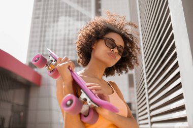 Duvarın yanında elinde kaykayla duran genç bir mulatta.