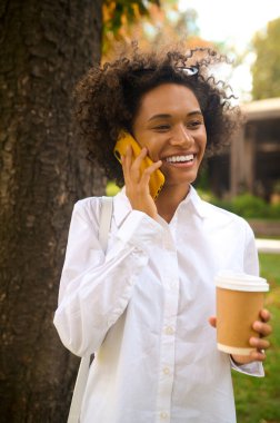 Kıvırcık saçlı bir kız telefonda konuşuyor ve memnun görünüyor.