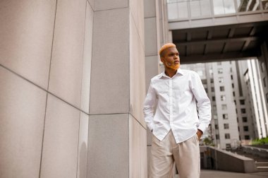 Beyaz elbiseli, koyu tenli genç adam kendinden emin görünüyor.