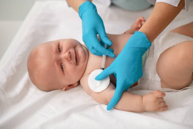 Sakin, sevimli bir bebek, bir sağlık uzmanı tarafından aşılanıyor.