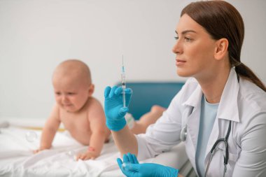 Doktor yeni doğmuş bir bebeğe iğne yapmaya hazırlanıyor.