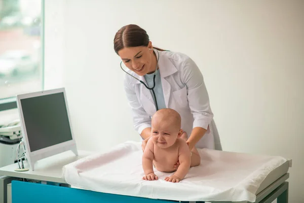 Médico experiente examinando uma criança perturbada com um estetoscópio estéril — Fotografia de Stock
