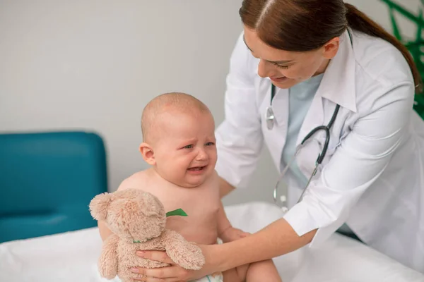Gondoskodó orvos játékot ad egy síró babának. — Stock Fotó