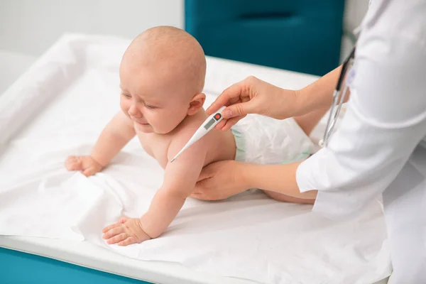 Mulher pediatra caucasiana experiente tomando a temperatura do bebê — Fotografia de Stock