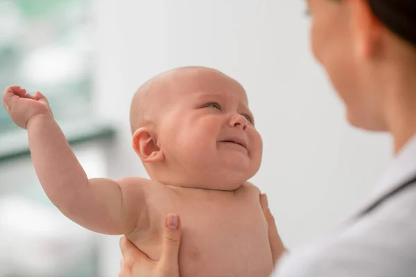 건강 진단을 받는 동안 소아과 의사를 보고 있는 슬픈 아기 — 스톡 사진