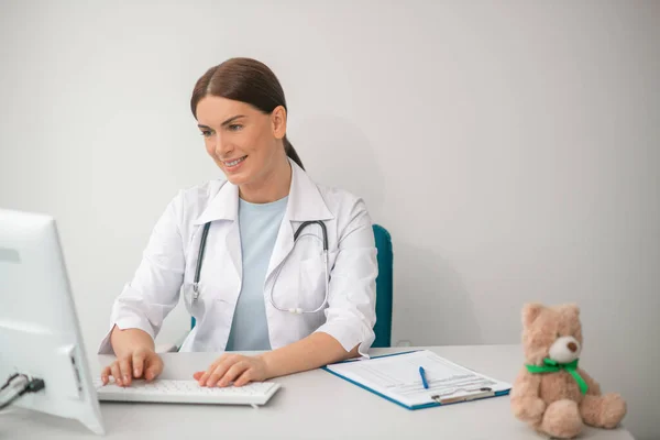 Μελαχρινή γυναίκα γιατρός με λευκή ρόμπα κάθεται στο γραφείο των γιατρών — Φωτογραφία Αρχείου
