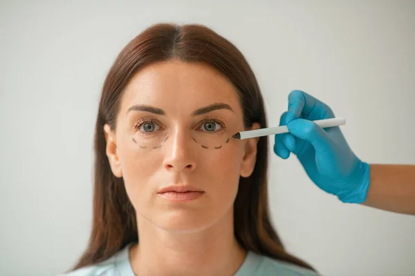 Cosmetoloog tekent lijnen op vrouwengezicht voor hijsprocedures — Stockfoto