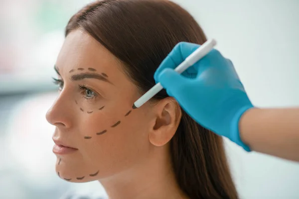 Kosmetikerin zeichnet Linien auf ein Frauengesicht — Stockfoto