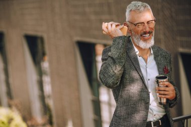 Gri saçlı, gözlüklü, sesli mesaj dinleyen bir adam.