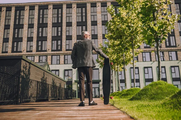 A mature man with a skateboard in the office district — Stock Photo, Image