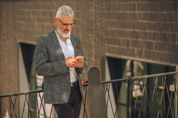 En mogen affärsman som står med en smartphone i handen — Stockfoto