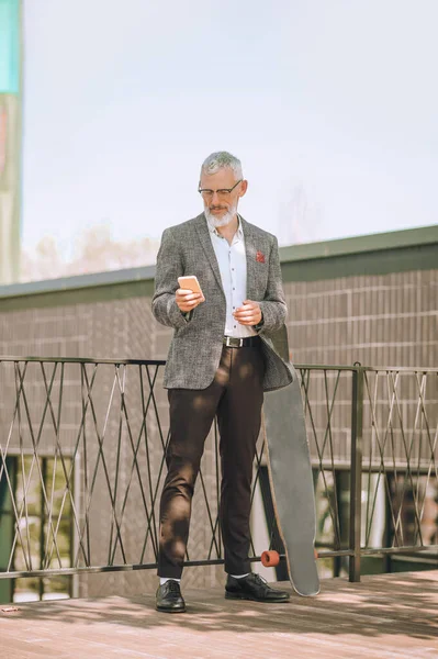En mogen affärsman som står med en smartphone i handen — Stockfoto