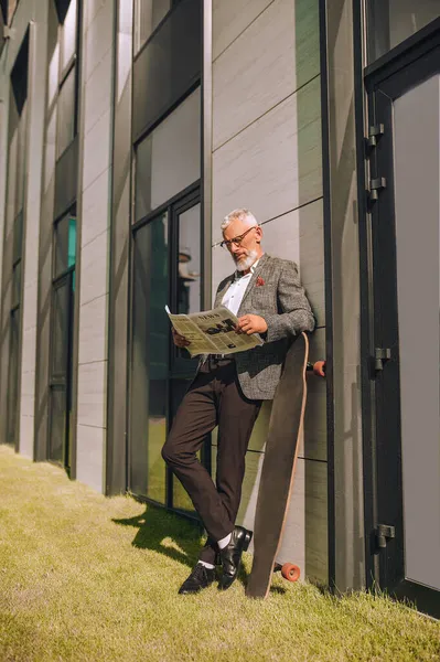 En gråhårig affärsman läser en tidning och ser involverad — Stockfoto