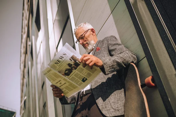 En gråhårig affärsman läser en tidning och ser koncentrerad ut — Stockfoto