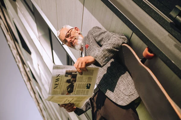 Gri saçlı bir işadamı gazete okuyor ve konsantre görünüyor.