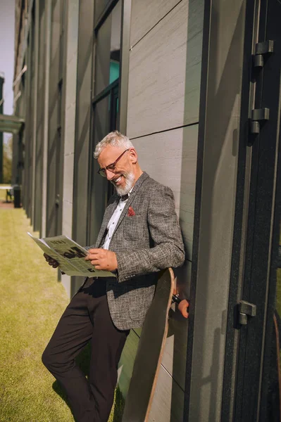 En gråhårig affärsman läser en tidning och ser involverad — Stockfoto