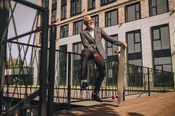 A mature businessman with a skateboard in the office district — Stock Photo, Image