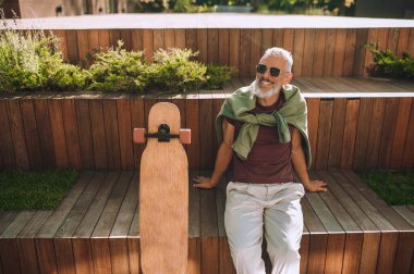 Güneş gözlüklü neşeli kaykaycı kaykay egzersizinden sonra dinleniyor.