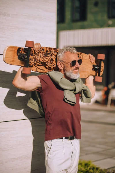 Güneş gözlüklü kaykaycı dışarıda duvarın yanında duruyor.