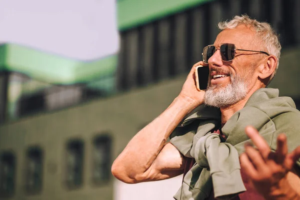 Glada gråhårig man som har ett telefonsamtal utomhus — Stockfoto