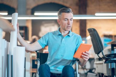 Tekerlekli sandalyedeki adam kağıdın yanındaki tablete bakıyor.