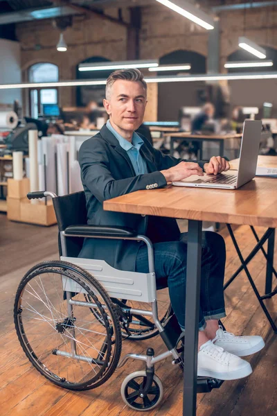 Чоловік в інвалідному візку за ноутбуком дивиться в бік — стокове фото