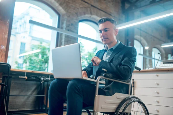 Людина з обмеженими можливостями у інвалідному візку, що працює на ноутбуці — стокове фото