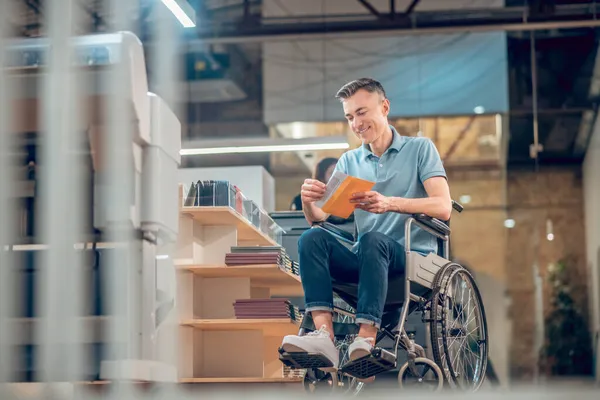 휠체어를 타고 엽서로 봉투를 보고 있는 행복 한 남자 — 스톡 사진