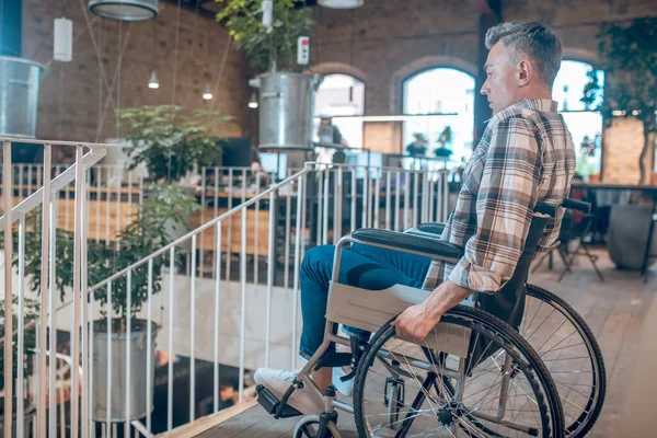 Man in profile on wheelchair looking desperately at stairs