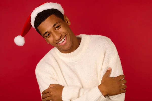 Joven chico sonriente en un suéter blanco y sombrero de santa — Foto de Stock