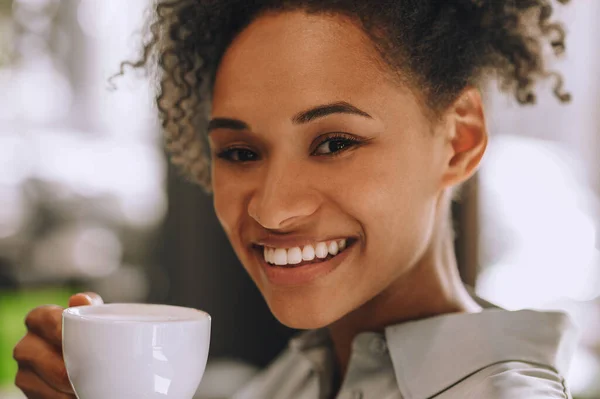 Mulher jovem de pele escura com uma xícara de café nas mãos — Fotografia de Stock