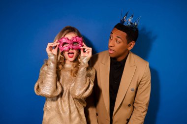 Taçlı bir adam maskeli bir kıza bakıyor.