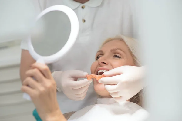 A female patient looking in the mirror at the results of the dental surgery — Foto Stock