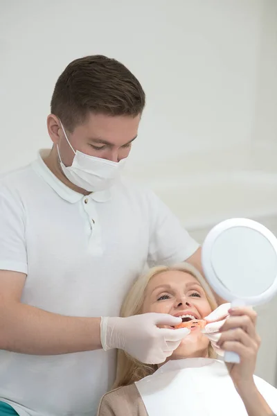 A female patient looking in the mirror at the results of the dental surgery — Foto Stock