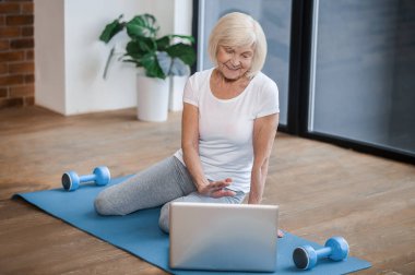 Gray-haired senior woman sitting on the floor and having a video call