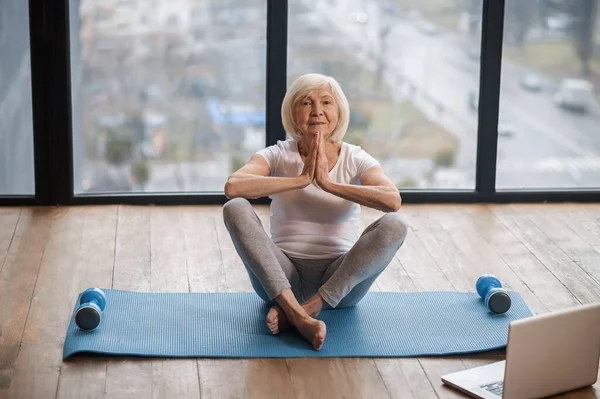 Gray-haired senior woman sitting on the floor and meditating — Stockfoto