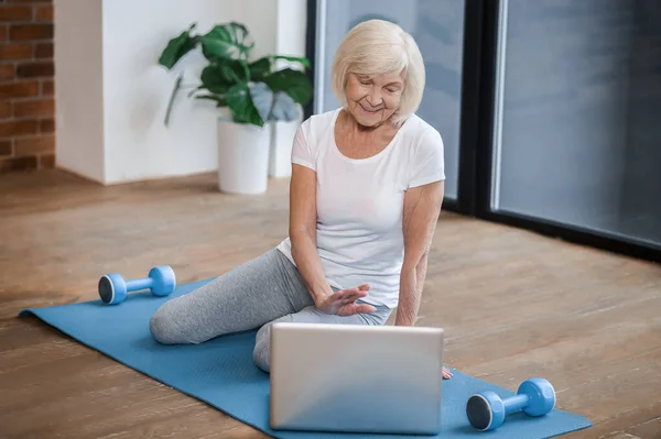 Grauhaarige Seniorin sitzt auf dem Boden und hat einen Videoanruf — Stockfoto