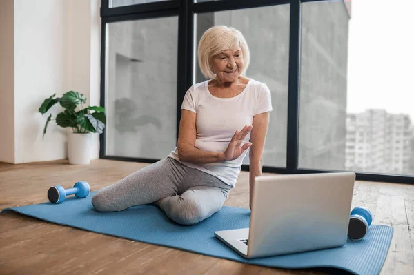 Gray-haired senior woman sitting on the floor and having a video call — Stockfoto